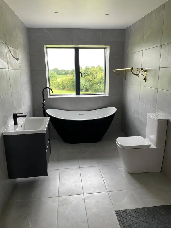 Renovated bathroom with grey marble-effect tiling, freestanding black bath and wall-hung vanity
