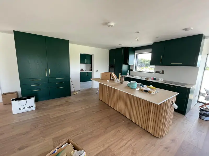 Newly fitted kitchen with dark green shaker units, brass handles and a fluted oak island