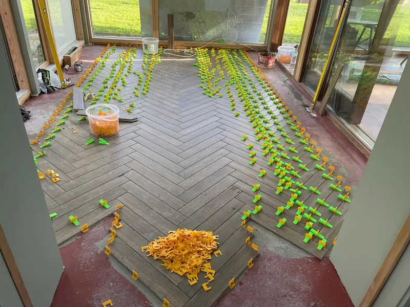 Herringbone floor tiling in progress with levelling clips and wedges set across the room