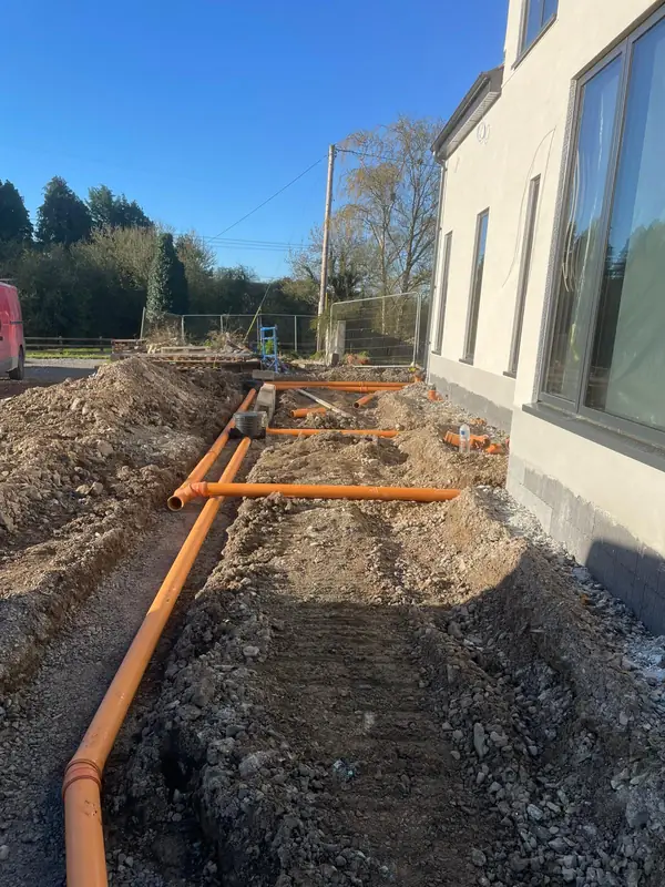 Open trenches with orange foul drainage pipework laid alongside a new build house