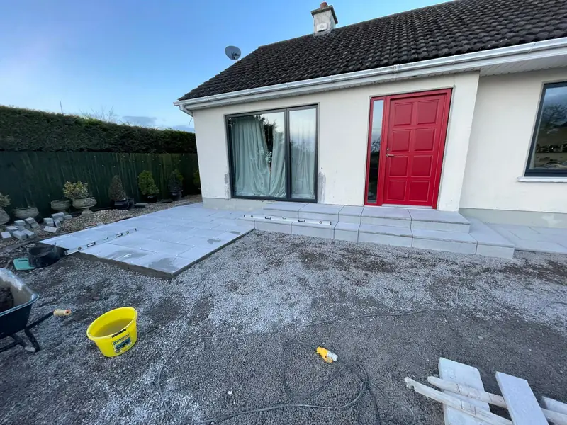 New granite paved patio and steps laid to the front of a bungalow with a red door