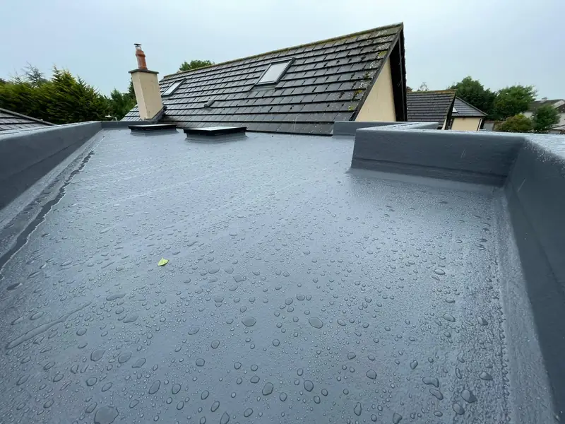 Close view of a finished GRP flat roof shedding rainwater, showing upstands and seamless corners